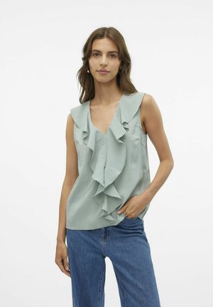 Lysegrøn ærmeløs top med V-hals og flæser foran. Blødt stof med en glat tekstur, bæres med blå jeans.