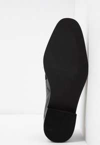 Semelle d'une chaussure habillée en cuir noir avec un talon léger, vue de dessous sur un fond blanc en coin.