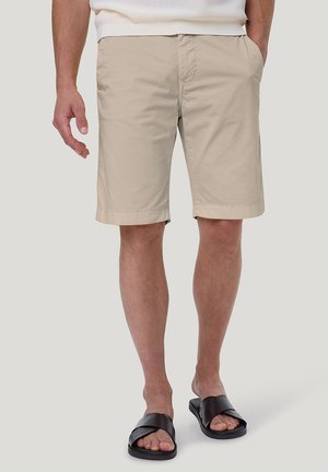 Beige Baumwollshorts mit flacher Vorderseite und Seitentaschen, in entspanntem Schnitt und mit gesäumten Bündchen, kombiniert mit schwarzen Riemchensandalen.