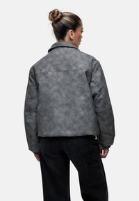 Giacca in finta pelle grigia con una finitura leggermente strutturata, dotata di colletto, spalle scese e dettagli del logo cuciti sul retro.