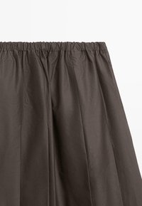 Dunkelbrauner Rock mit elastischem Bund und einem gerafften Design, gefertigt aus einem glatten, leichten Stoff mit dezentem Glanz.