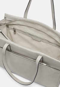 Szara skórzana torba typu tote z zasuwaną kieszenią wewnętrzną, gładka faktura, dwa uchwyty i minimalistyczny design. Wnętrze wykończone jest jasnym materiałem.