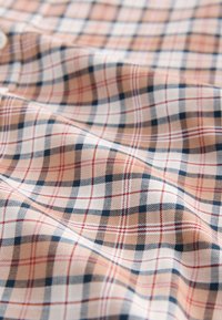 Tissu à carreaux en pêche, blanc et bleu marine. Présente un tissage texturé avec un motif classique de carrés et de lignes alternés.