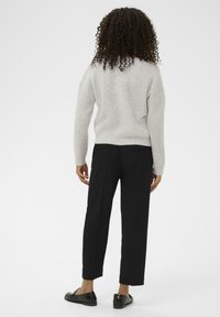 Grå stickad tröja med ribbad textur, svarta skräddarsydda byxor med rak passform och svarta slip-on skor. Bakgrunden är helt vit.