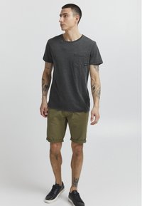 Grå t-shirt med korte ærmer og brystlomme, parret med opkrøllede olivengrønne shorts og sorte sneakers, der har et minimalistisk design.