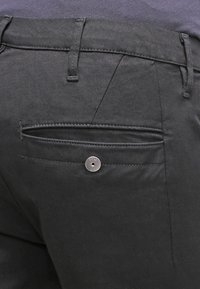 Czarne spodnie o gładkiej fakturze, z tylną kieszenią z haftowanym brzegiem i srebrnym guzikiem zwracającym uwagę na górnym prawym rogu.