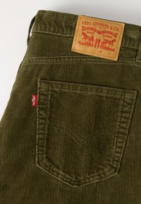 Παντελόνι Levi's από βελούρ σε ελιά πράσινη απόχρωση, με πίσω τσέπη που έχει κόκκινη ετικέτα Levi's και δερμάτινη ετικέτα Levi Strauss & Co. στο ζωνάρι σε ταμπά απόχρωση.