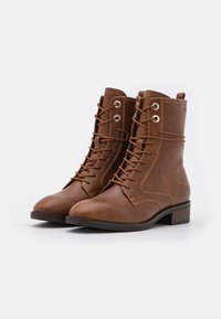 Braune Leder-Ankle-Boots mit abgerundeter Spitze, Schnürung auf der Vorderseite, Metallösen und einem niedrigen Blockabsatz. Seitliche Nahtdetails sind sichtbar.