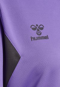 Fioletowa koszulka sportowa z fakturowanej tkaniny, z czarnym trójkątnym akcentem i czarnym logo z wzorem pszczoły.