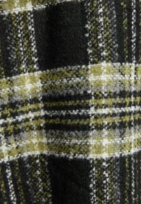 Černá a olivově zelená kostkovaná tkanina s jemnou, chlupatou texturou a bílými liniemi, které se protínají v klasickém vzoru kostiček.