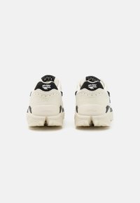 Beige and black footwear with a cushioned sole, rounded shape, suede and mesh material, featuring the HI-TEC logo on the heel.