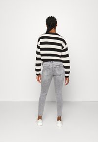 Pull court à rayures noires et blanches avec des manches longues, associé à un jean skinny taille haute gris clair et des baskets blanches.