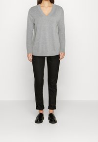 Grauer V-Ausschnitt-Pullover mit langen Ärmeln, aus weichem Stoff. Kombiniert mit schwarzen, taillierten Hosen und schwarzen Slippern. Einfaches Design, ohne Muster.