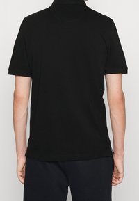 Polo shirt nera con maniche corte, colletto classico e tessuto a maglia liscio con una vestibilità morbida.