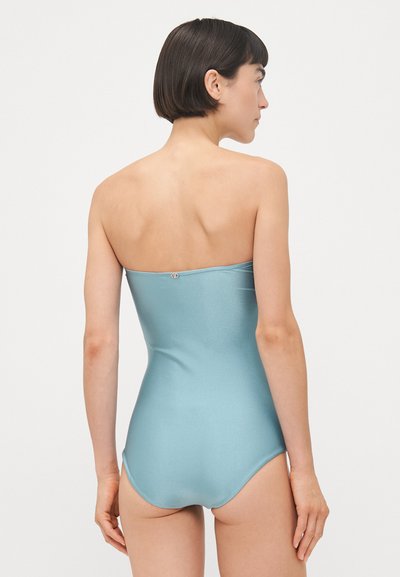 Costum de baie unei piese, fără bretele, de culoare albastru deschis, realizat dintr-un material neted și lucios. Prezentă un închizător subtil la spate și un design adaptat.