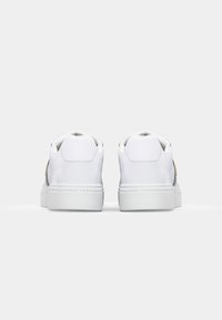 Zapatillas de cuero blanco con un acabado liso, suela blanca plana y un sutil logotipo en el lateral. Tacón redondeado y diseño minimalista.