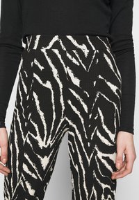 Svart-och-vitrandiga byxor med en texturerad tyg, med ett zigzag-mönster. Hög midja med veck och en avslappnad passform.