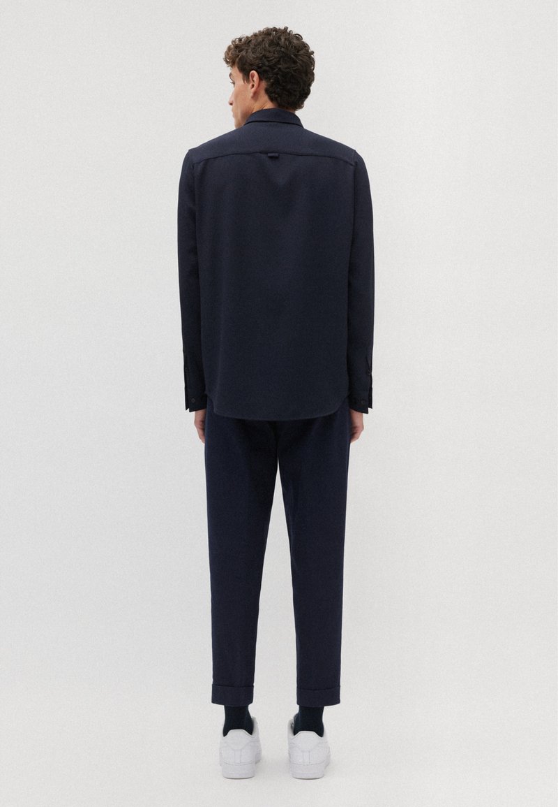 Marineblauses Hemd mit einem Rückenschlitz, langen Ärmeln und Knopfmanschetten, kombiniert mit schmal geschnittenen marineblauen Hosen und weißen Turnschuhen.