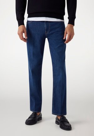 Dark blue denim jeans with a straight fit, accentuated seams, and a classic five-pocket design. Paired with black leather loafers.