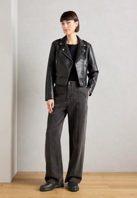 Veste courte en cuir noir avec quincaillerie argentée, associée à un pantalon large taille haute gris foncé et des chaussures noires épaisses avec des accents de chaîne.