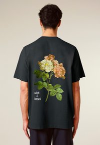 Black cotton t-shirt featuring a floral design of roses in peach and cream hues, with green leaves and the text "LOVE & ROSES."