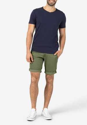 Navyblaues V-Ausschnitt-T-Shirt kombiniert mit locker gerollten olivgrünen Shorts und weißen Sneakern. Baumwollmaterial mit lässigem Design.