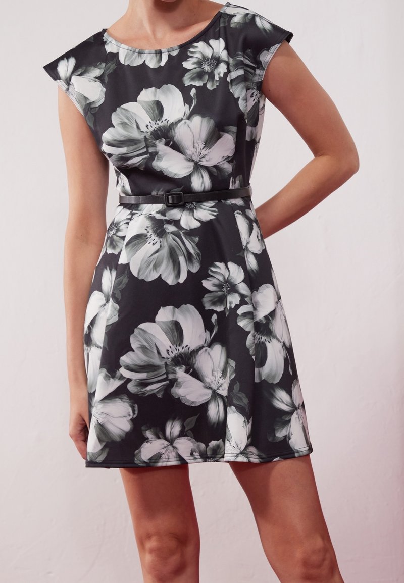 Vestido de tela con estampado floral en blanco y negro, con mangas cortas y un cinturón ajustado en la cintura, creando una silueta acampanada.