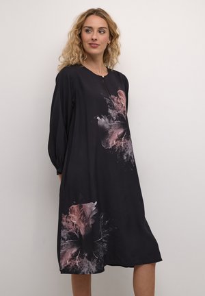Vestido negro de manga larga, con patrones abstractos de flores en rosa. Tejido suave, corte relajado y escote redondo con un sutil detalle de cierre.