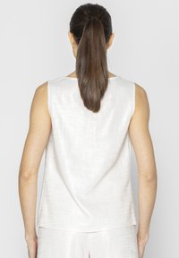 Bez rękawów top w jasnobeżowym materiale o teksturowanym wykończeniu, z luźnym krojem i nieco dłuższym tylnym brzegiem.