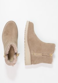 Botas de tobillo de ante beige con forro de piel sintética, cierre de cremallera lateral y suela de goma texturizada. Superficie lisa con diseño minimalista.