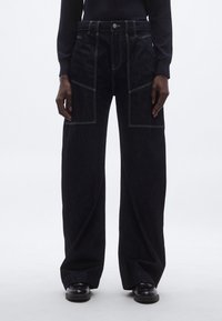 Hlače širokih nogavica od tamnog trapera s prednjim džepovima, kontrastnim šavovima i visokim strukom. Teksturirani materijal s glatkim završetkom.