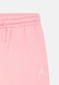 Ružové teplákové nohavice s elastickým pásom a šnúrkou, so malým bielym logom Jumpman na pravej strane blízko vrecka.