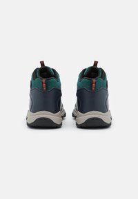 Ein Paar grüne und marineblaue Wanderschuhe von hinten betrachtet, mit grauen Sohlen und orangefarbenen Schlaufen auf einem weißen Hintergrund.