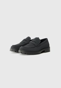 Sorte slip-on sko med gummisåle, glatt tekstur, bred tupp, og to horisontale stropper over toppen. Forsterket sømdetalj.