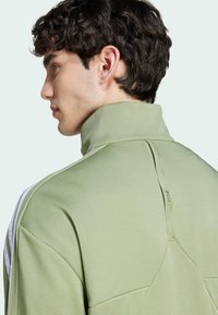 Felpa verde con colletto alto, caratterizzata da un dettaglio con cucitura posteriore e strisce bianche sulle spalle. Materiale in morbido cotone misto.