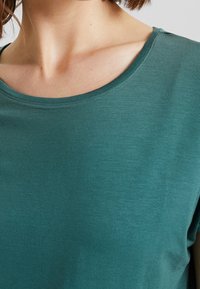 Teal kortärmad t-shirt med rund halsringning. Mjuk, lätt tyg med en slät textur. Sömsdetaljer vid halsringningen.