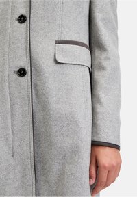 Grauer Wollmantel mit Fischgrätmuster, Knopfverschluss, schwarzen Knöpfen und braunen Verzierungen an Taschen und Ärmelsäumen.