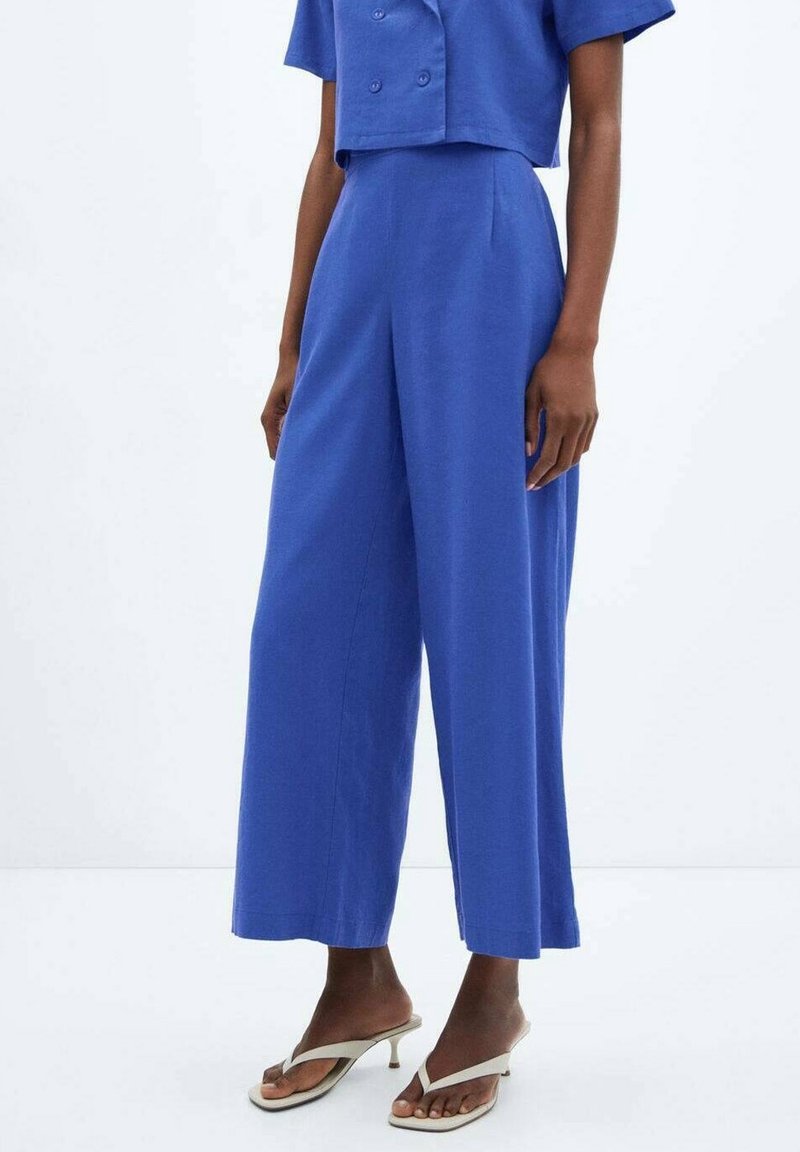 Pantalon large bleu en tissu léger, avec une taille haute et des plis sur le devant. Associé à un haut assorti à manches courtes.