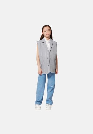 Blazer sin mangas a rayas grises con dos bolsillos frontales, combinado con jeans de color azul claro y zapatillas blancas, usado por un joven modelo.