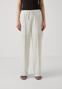Pantalons larges légers en tissu crème doux. Dotés d'une taille à cordon de serrage et d'une finition texturée. Assortis à des sandales noires.