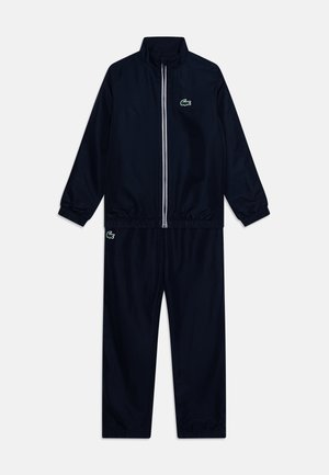 Survêtement bleu marine en tissu doux, composé d'une veste zippée avec un col haut et des poignets élastiques, assorti à un pantalon fuselé. Détail de logo vert.