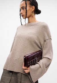 Μπεζ πουλόβερ με φαρδιές μανίκες και ριγωτή τελείωση, συνδυασμένο με μπορντό τσάντα clutch με ασημί μεταλλικά στοιχεία και σχέδιο με καρφιά.