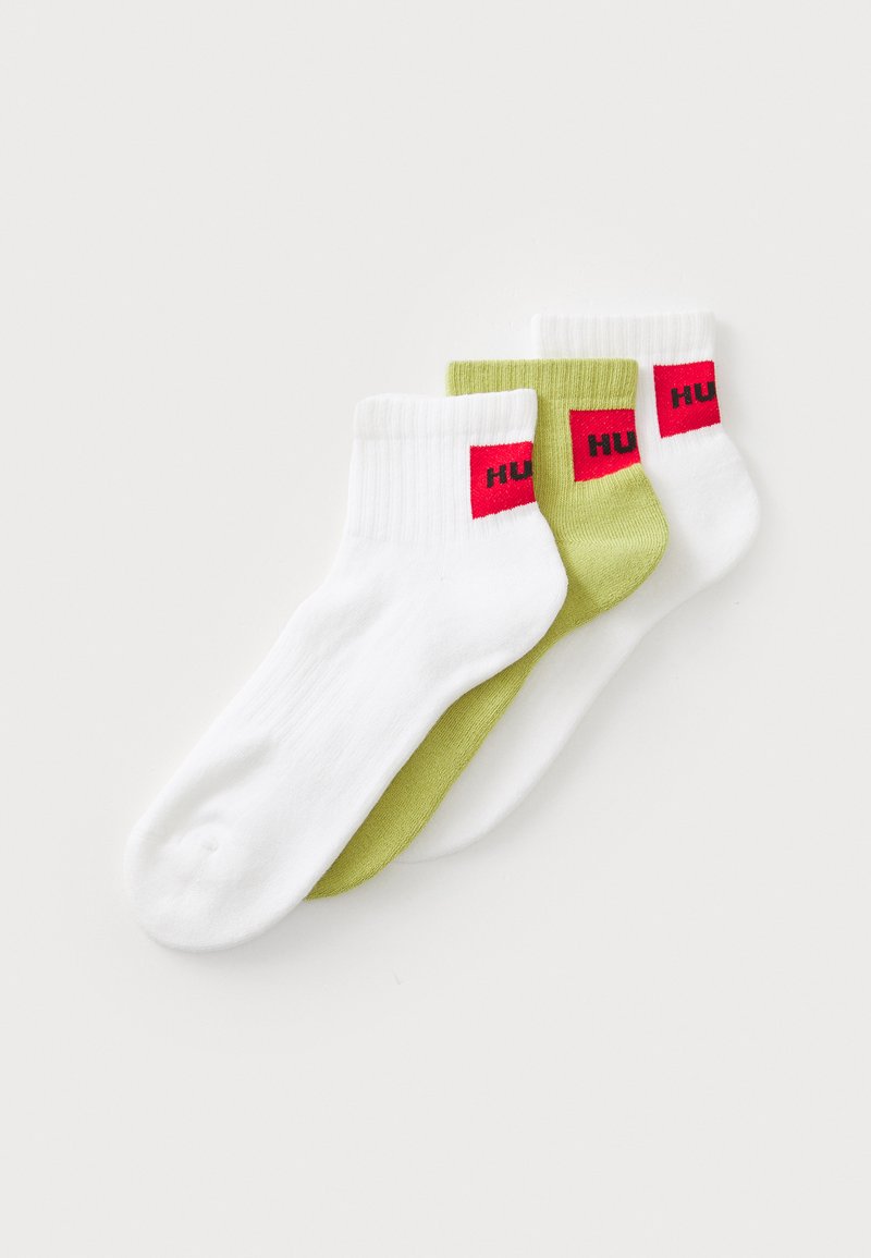 Trois paires de chaussettes de cheville : deux blanches avec un logo rouge et une verte. Fabriquées en tissu doux, avec des bords côtelés et une texture lisse.