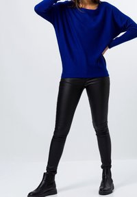 Pull bleu surdimensionné associé à un pantalon skinny en cuir noir et des bottines. Le pull présente un large décolleté et des manches longues.