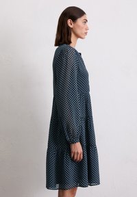Navy jurk met bloemenpatroon, lange, opbollende mouwen en een tiered zoom. Gemaakt van lichte stof, met een knoopsluiting bij de hals en een losse pasvorm.