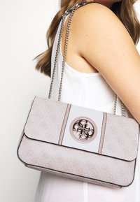 Light pink handbag with a patterned exterior and metal logo. Features a chain strap and flap closure with a smooth leather accent.