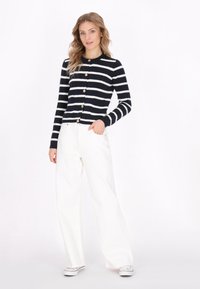 Cardigan a righe blu navy e bianche con bottoni dorati, abbinato a pantaloni bianchi a gamba larga. Il tessuto appare morbido con una finitura testurizzata.