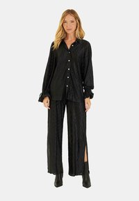 Czarny zestaw z tkaniny krepy, składający się z koszuli zapinanej na guziki z długimi rękawami oraz spodni z rozkloszowanymi nogawkami i bocznymi rozcięciami. Całość ma teksturowany wzór.