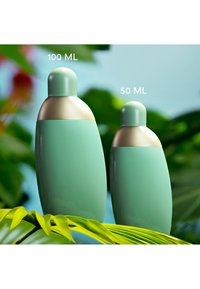 To grønne og gyldne runde flasker mærket 100 ML og 50 ML stående på grønne blade med en sløret naturlig baggrund.