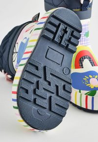 Mehrfarbige Gummistiefel mit einem marineblauen Obermaterial, strukturiertem Boden und gemustertem Sohlenrand mit Streifen und floralem Design.